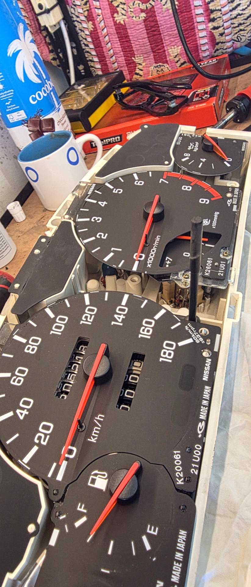 Nissan Skyline gauge cluster fully disassembled on workbench showing speedometer, tachometer, and fuel gauges