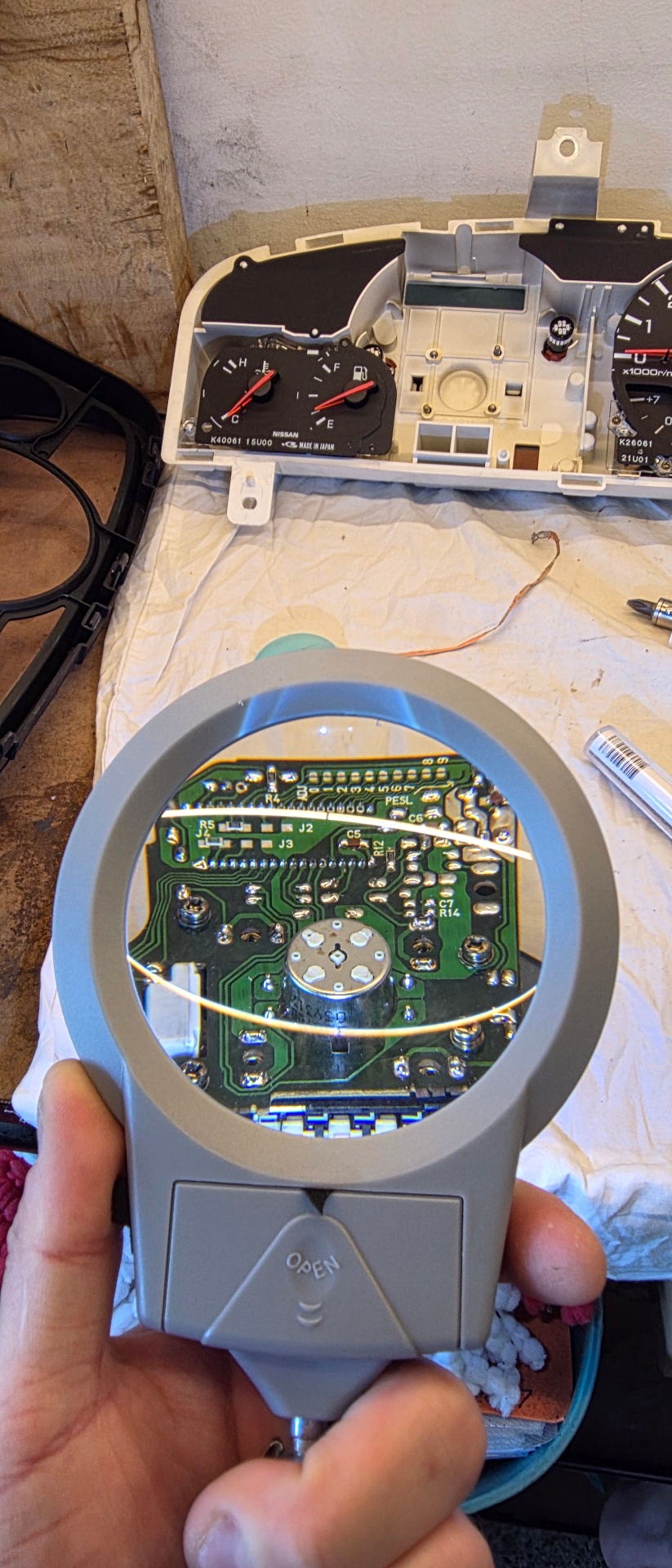 Nissan cluster PCB inspected under illuminated magnifier showing solder joint detail